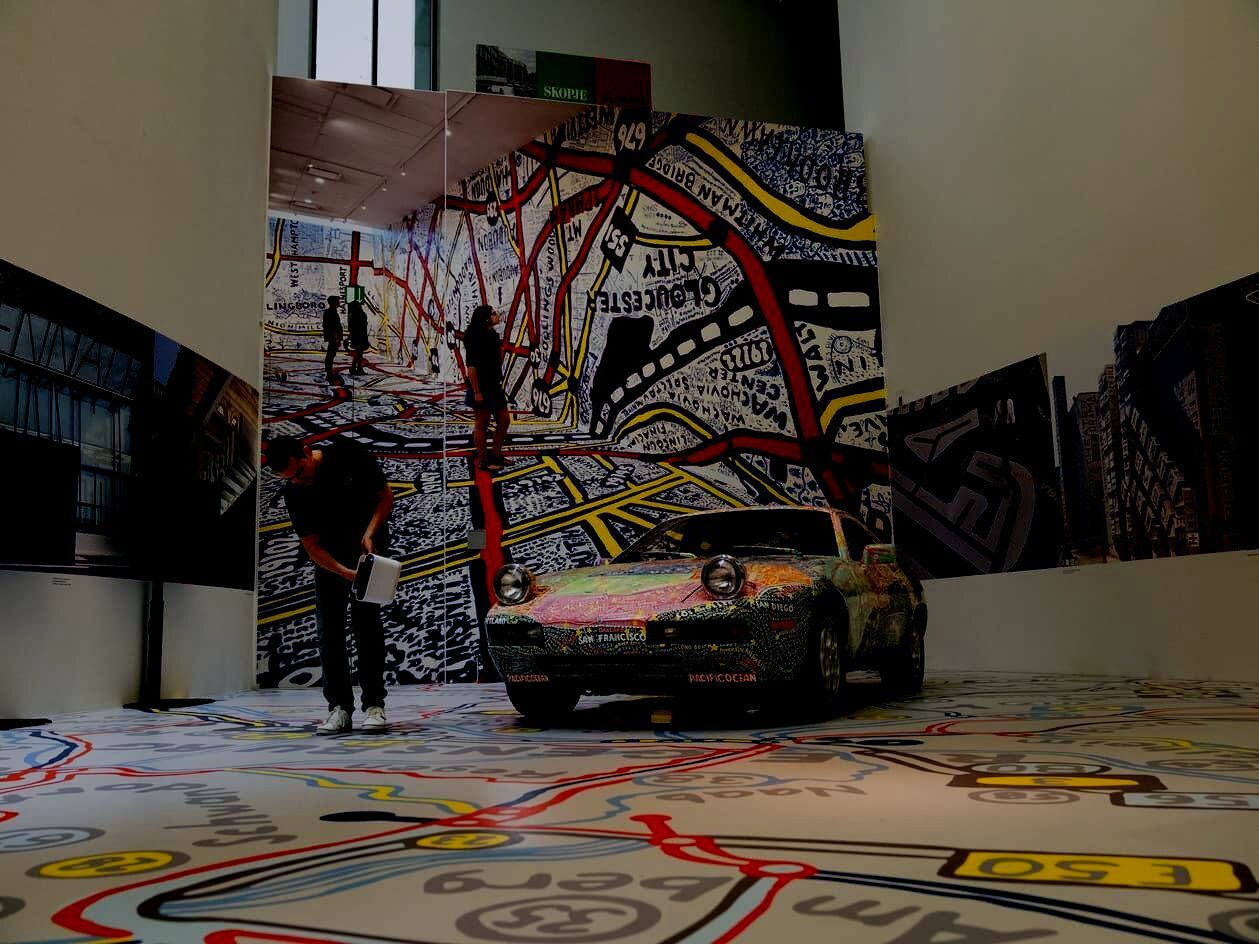 A Porsche 928 fully wrapped in a hand-drawn city map mural inside an immersive gallery installation